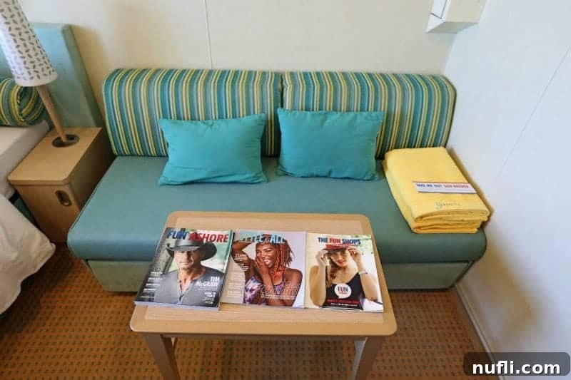 Comfortable couch with yellow towels, Carnival magazines, and a nightstand in a Cloud 9 Spa Stateroom