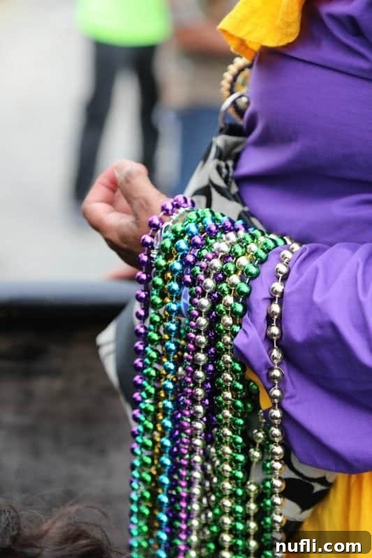 Close-up of a woman's arm, heavily draped with multiple strands of vibrant Mardi Gras beads, symbolizing the festive bounty.