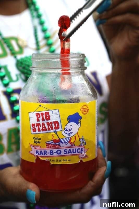 A hand reaching into a 'Pig Stand Bar-B-Q Sauce' jar, retrieving a glistening tequila gummy worm, a quirky treat for the celebration.