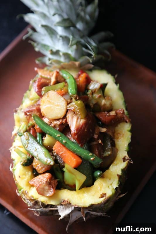 a pineapple filled with teriyaki chicken and vegetables on a wooden plate