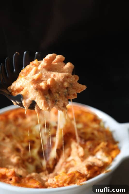 A dark pasta server scooping a generous portion of cheesy ziti from a white baking dish, highlighting the melted and bubbly cheese and perfectly cooked pasta.