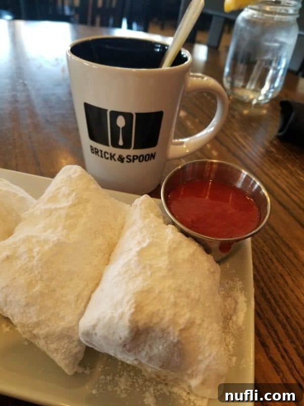 A generous serving of Brick & Spoon's classic beignets, lightly dusted with powdered sugar, set in front of a branded mug.