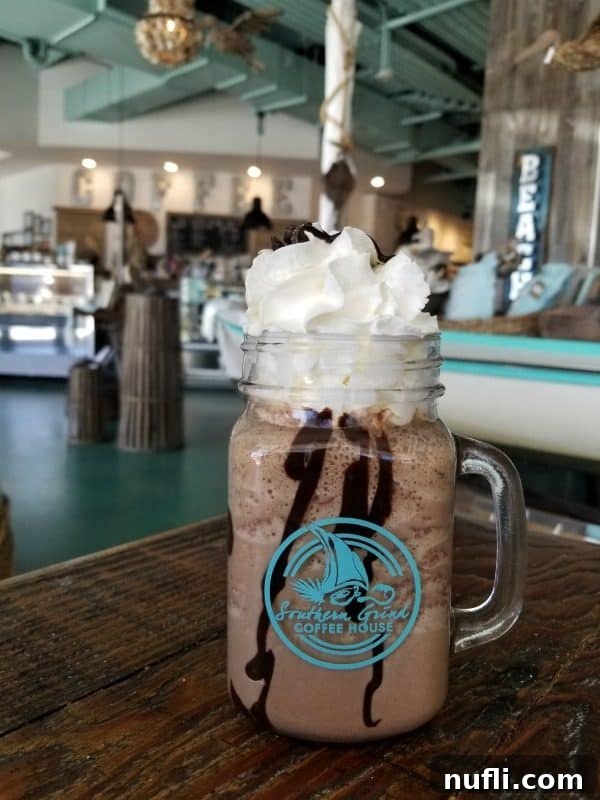 An inviting iced coffee generously topped with a swirl of whipped cream and a rich chocolate sauce, served in a Southern Grind Coffee House branded mug.