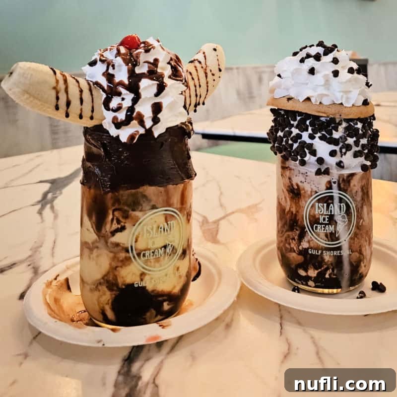Two elaborate milkshakes served in mason jars, lavishly topped with whipped cream, various sweets, and colorful garnishes, highlighting the decadent offerings of Island Ice Cream and Treats.