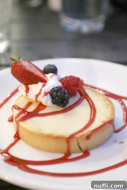 A delicate key lime tart adorned with fresh berries and a dollop of whipped cream, presented on a pristine white plate, capturing the elegance of Coast Restaurant's dessert.
