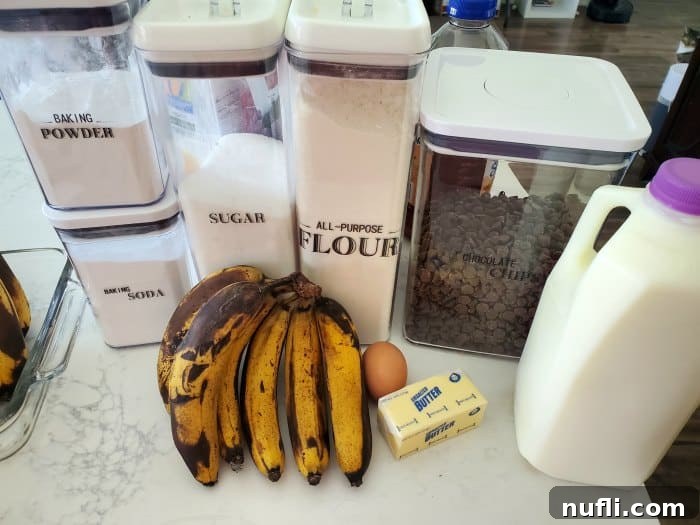 All ingredients for Chocolate Chip Banana Bread laid out on a kitchen counter: baking powder, baking soda, sugar, flour, chocolate chips, bananas, an egg, butter, and milk.