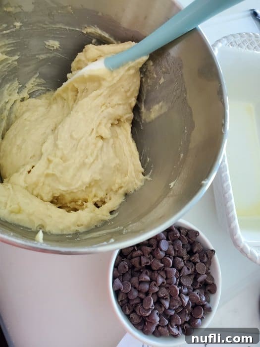 Banana bread batter in a metal bowl with a spatula, next to a smaller bowl of chocolate chips.