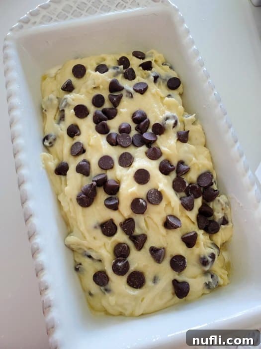 Chocolate chip banana bread batter ready in a white bread pan, with a few extra chocolate chips sprinkled on top.