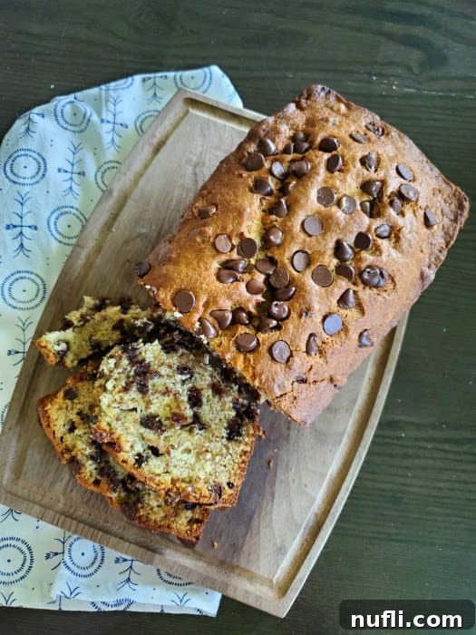 Sliced Chocolate Chip Banana Bread on a wooden cutting board next to a cloth napkin, showing the moist interior and melted chocolate chips.