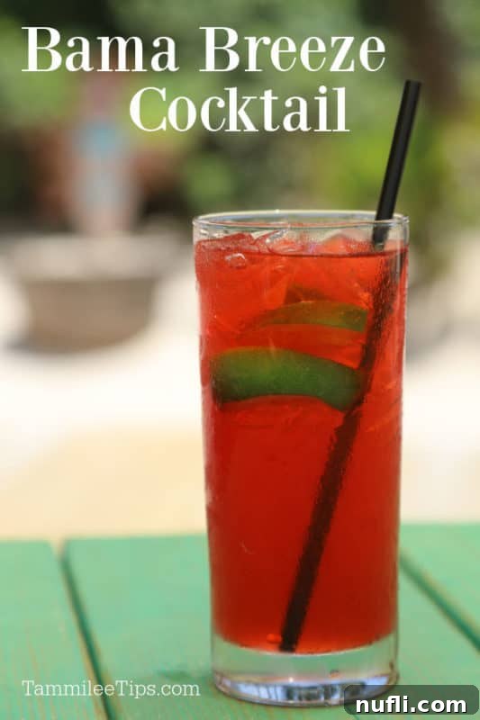 A vibrant red Bama Breeze cocktail garnished with fresh lime slices, presented in a tall glass, evoking the refreshing spirit of Alabama's Gulf Coast.