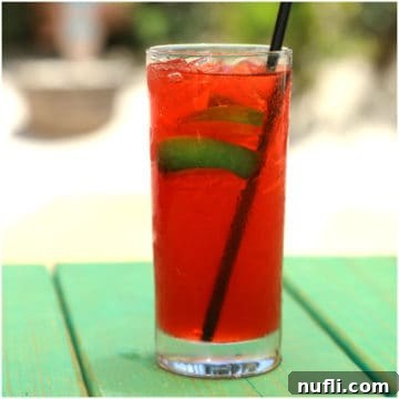 A refreshing red cocktail with lime slices in a tall glass, set on a green picnic table, embodying relaxation and enjoyment.