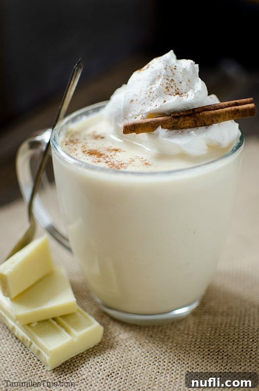 White hot chocolate garnished with whipped cream and a cinnamon stick in a glass coffee mug, a perfect holiday drink.