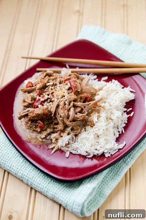 a red plate with Thai pork and rice next to chopsticks on a cloth napkin