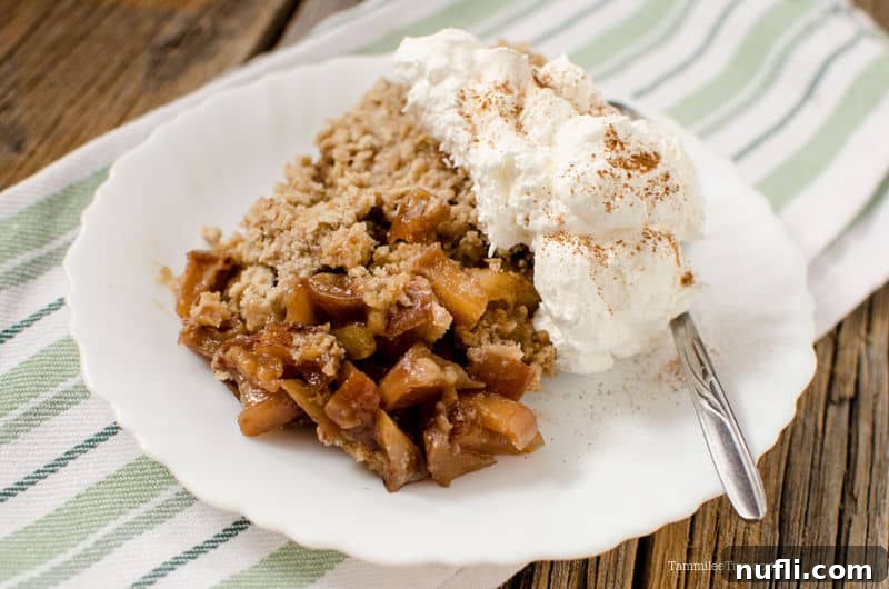 Decadent Crock Pot Caramel Apple Crisp 3 Warm caramel apple crisp with a scoop of vanilla ice cream and a spoon on a white plate.