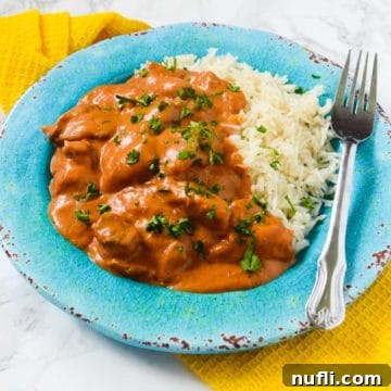 Chicken Tikka Masala next to white rice on a blue plate on a yellow cloth napkin