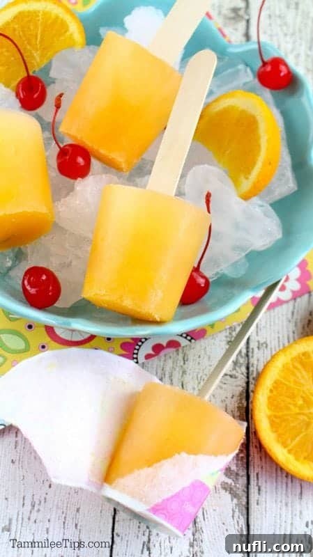 Orange popsicles in a bowl filled with ice and maraschino cherries and orange wedges