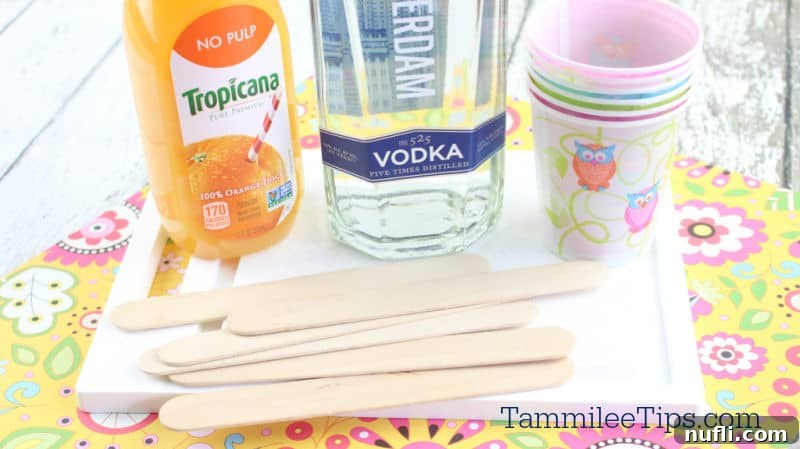 A bottle of Tropicana orange juice, vodka, along with paper cups and popsicle sticks.