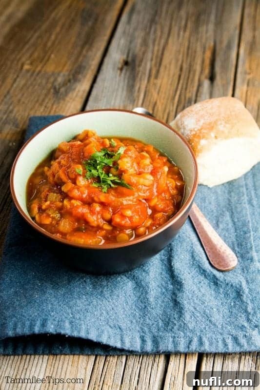 A beautifully presented bowl of vegan lentil soup, accompanied by a crusty bread roll and a spoon, on a patterned napkin.