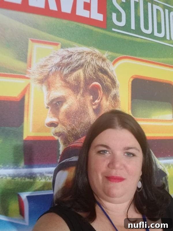 Tammilee standing next to a poster of Chris Hemsworth, smiling and pointing