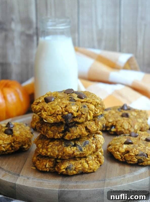 Stack of oatmeal cookies on a wooden board with a pumpkin and glass of milk in the background