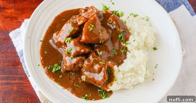 Close-up of beef tips covered in rich gravy next to fluffy mashed potatoes on a white plate