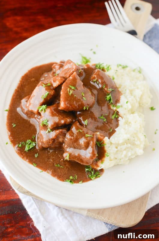 Beef Tips and Gravy on a white plate next to mashed potatoes, ready for a delicious meal