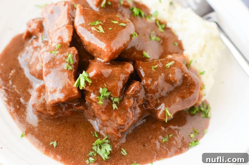 Close-up of beef tips smothered in gravy next to mashed potatoes on a white plate, highlighting the rich texture