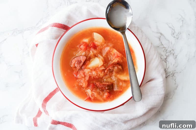 sausage sauerkraut soup in a white bowl with a spoon on it. 