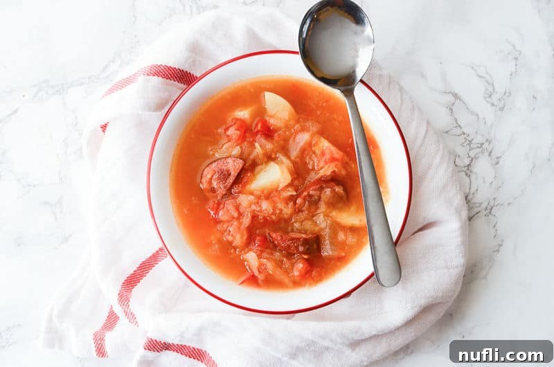 Sausage sauerkraut soup in a white bowl with a spoon on it. 