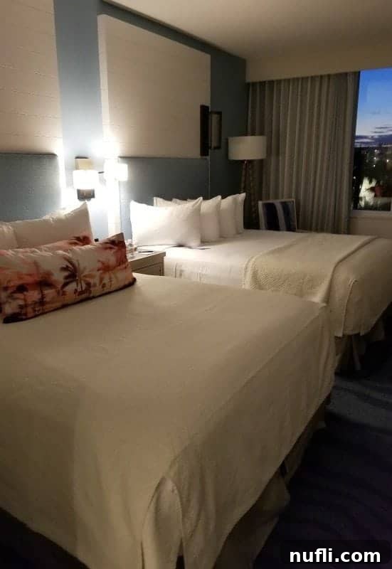 Two comfortable queen beds with tropical-themed pillows and modern furnishings in a Sapphire Falls guest room