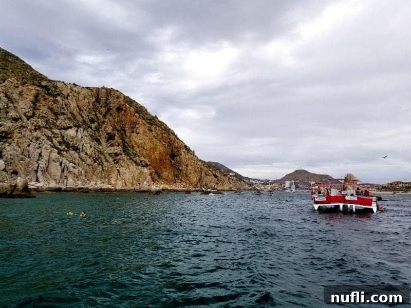 Cabo San Lucas Sail and Snorkel Bash 5 Several people snorkeling near unique rock formations, with a bright red boat anchored nearby, showcasing the vibrant marine environment.
