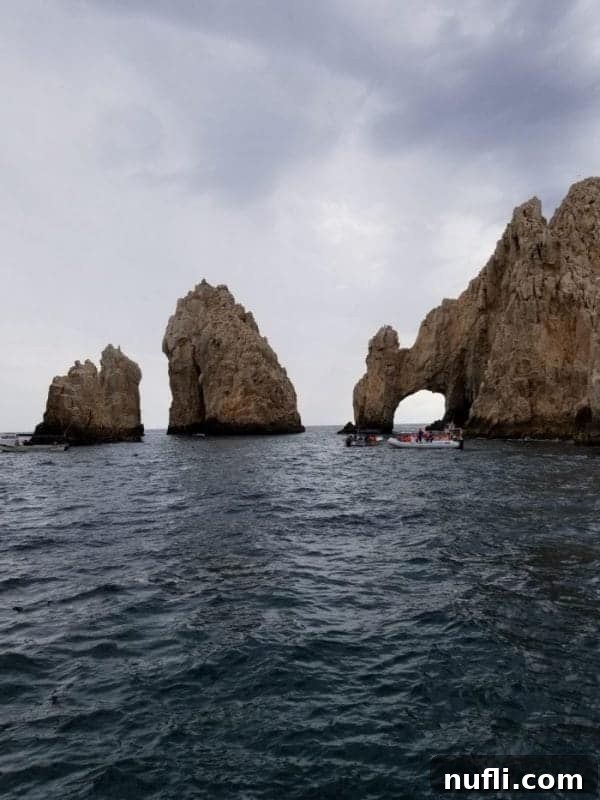 Cabo San Lucas Sail and Snorkel Bash 6 The iconic Los Arcos natural rock formations at Land's End in Cabo San Lucas, with several boats cruising nearby under a clear sky.