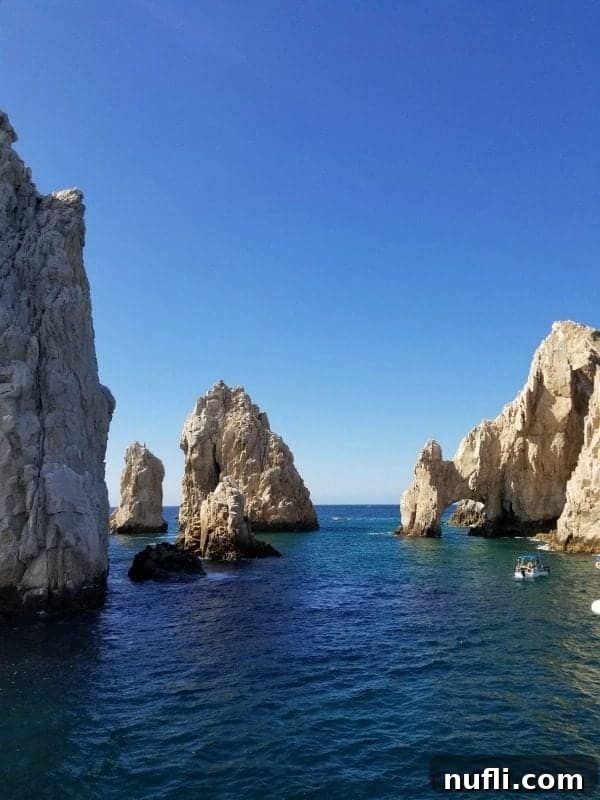 The iconic El Arco (The Arch) rock formation in Cabo San Lucas with a tour boat passing nearby.