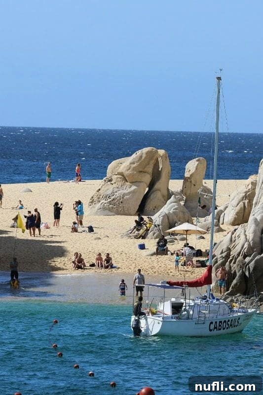 People enjoying Lovers Beach next to a Cabo Sails sailboat, a popular destination in Cabo San Lucas.