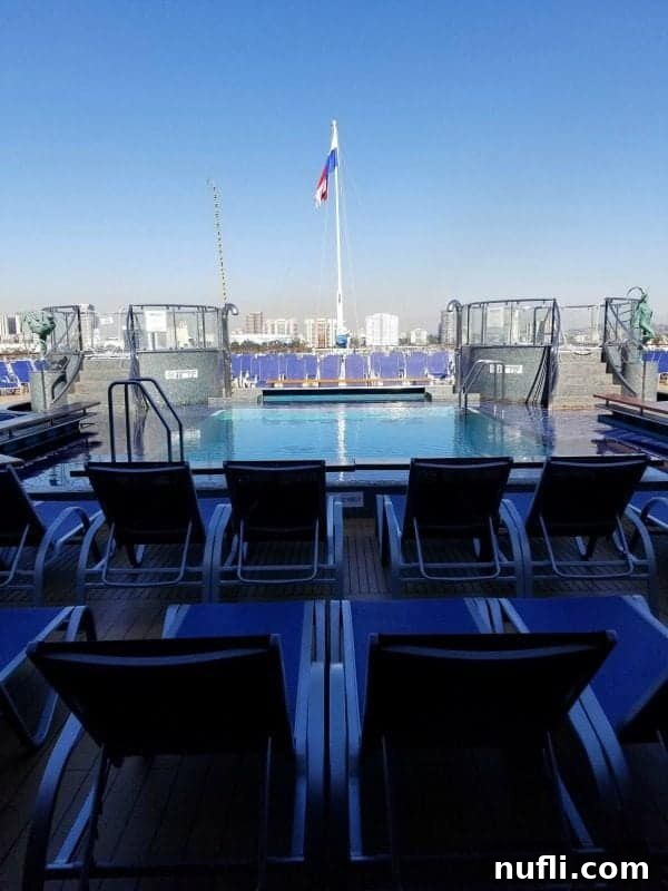 A spacious pool surrounded by comfortable blue chairs, with the ship's flag gently waving at the far end, offering a serene view.