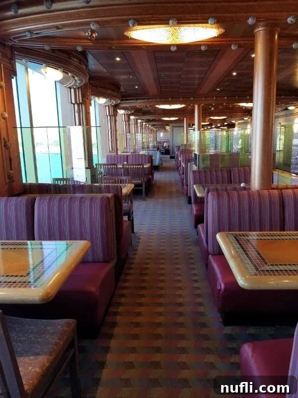 Long rows of comfortable booths and tables situated near large windows, offering picturesque views on the Carnival Splendor.
