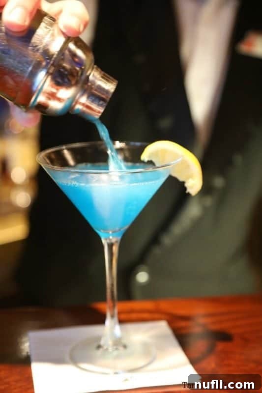 bartender pouring a sea blue martini into a martini glass