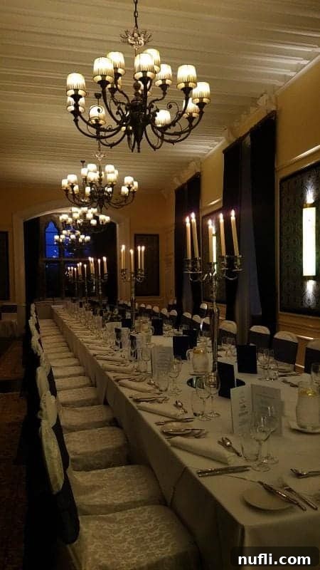 Dining room with a long table lit by candles under chandeliers 