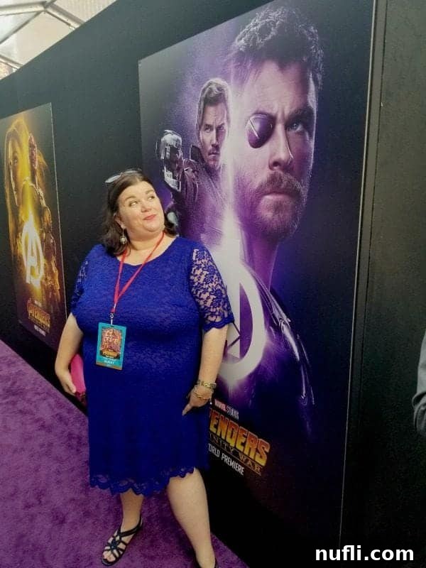 Blogger Tammilee posing next to a vibrant Marvel Avengers Infinity War promotional poster at the premiere.