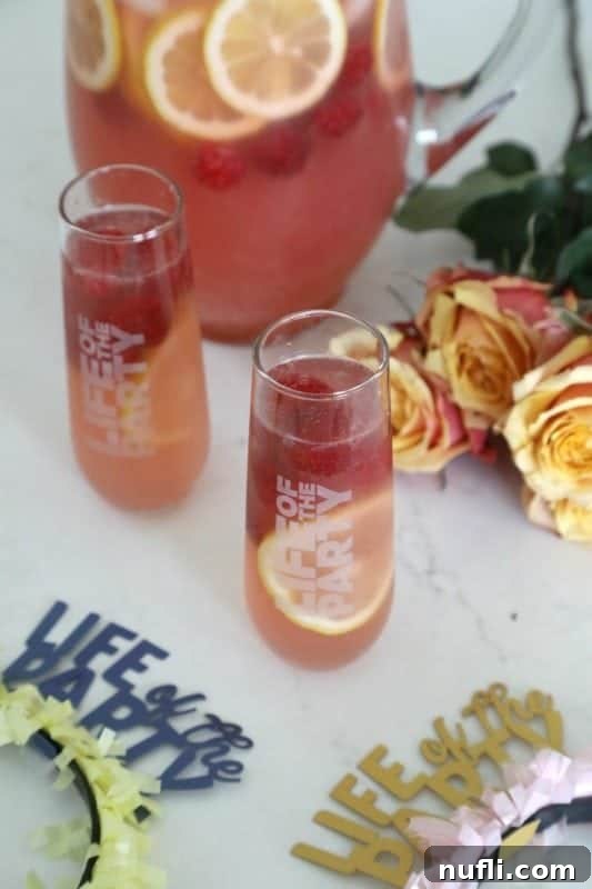 Beautifully presented 'Life of the Party' themed glasses filled with Raspberry Lemonade Moscato Punch, garnished with fresh raspberries and lemon slices, beside a pitcher and elegant roses.