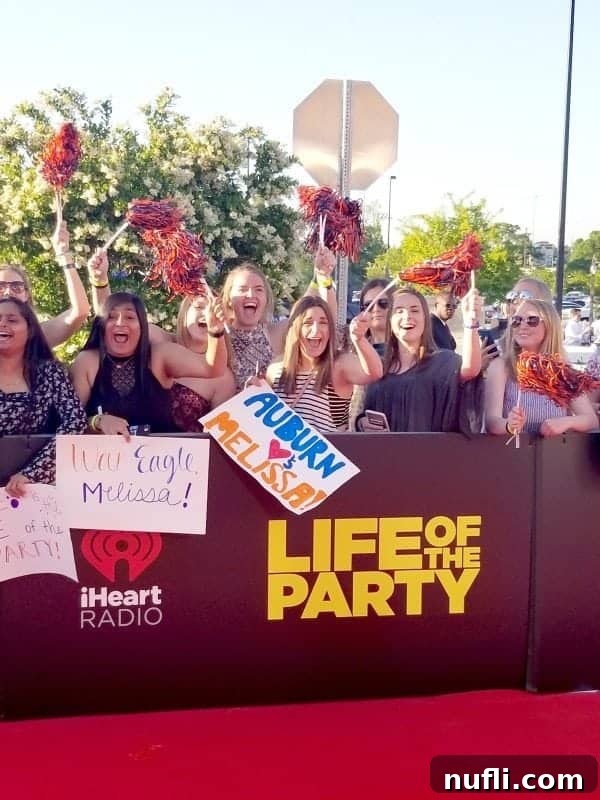 Enthusiastic crowd of Auburn University students holding pom-poms and signs, gathered around a large 'Life of the Party' movie premiere display, celebrating the event.