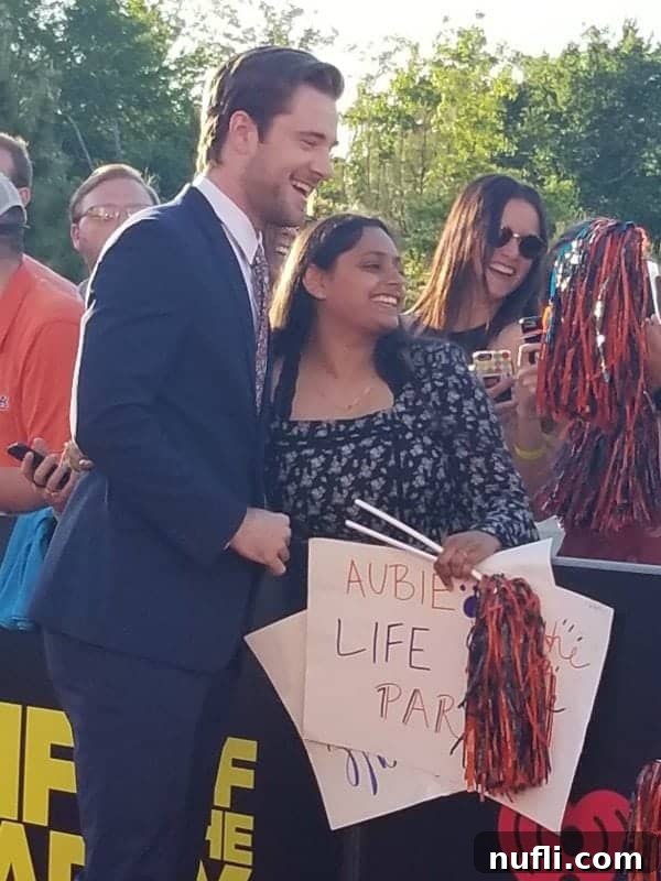 Actor Luke Benward warmly greeting a fan on the 'Life of the Party' red carpet at Auburn University, with a movie sign visible in the background.