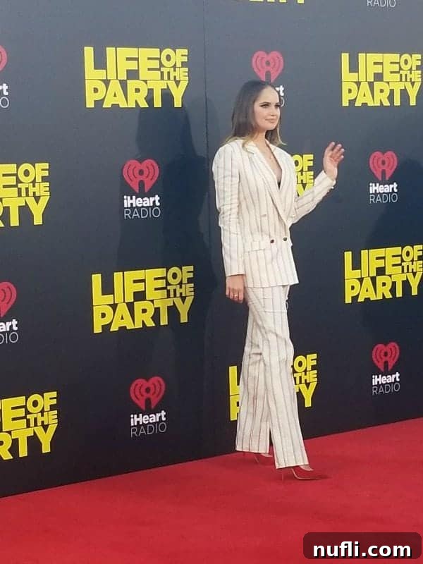 Debby Ryan posing gracefully next to a 'Life of the Party' movie premiere sign, captivating the red carpet audience.