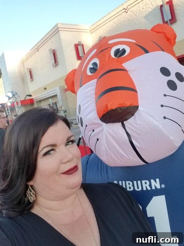 Tammilee from Tammilee Tips, smiling brightly next to a large inflatable Auburn Tigers mascot, showcasing the vibrant school spirit at the movie premiere.