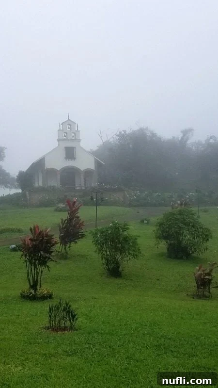 A quaint church standing in the distance, partially obscured by fog and clouds on a misty day, creating an ethereal scene.