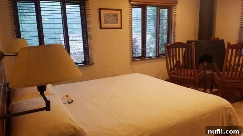 The interior of a Villa Blanca casita, featuring a comfortable bed with crisp white linens, a stone fireplace, and two rustic rocking chairs.