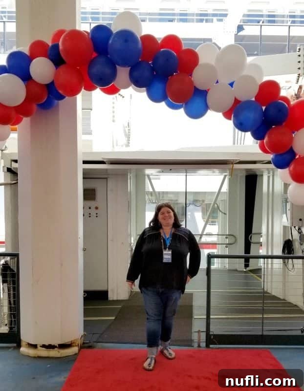 Tammilee standing happily under a festive red, white, and blue balloon arch on the Carnival Horizon, celebrating the inaugural event