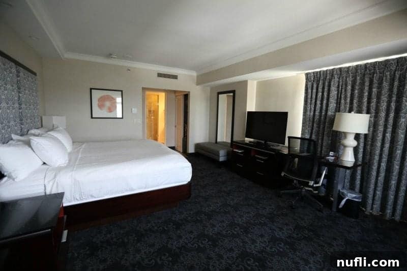 Spacious hotel room featuring a king bed, television, and elegant lamp on a long console