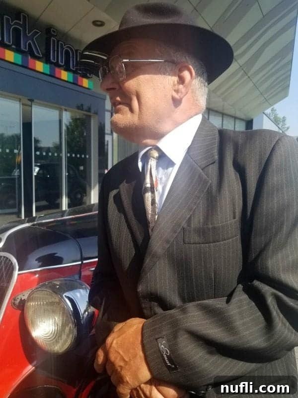 dapper gentleman in a pin stripe suit and hat leaning against a historic car