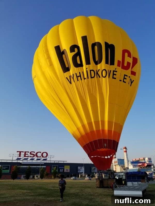 The Balon.cz hot air balloon, a striking yellow and orange, fully inflated and ready for launch in the Tesco parking lot.